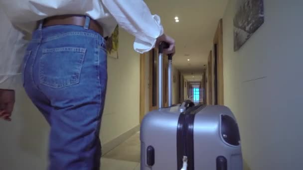 Zadní pohled na ženu kráčející chodbou hotelu. kutálí si zavazadla za sebou — Stock video