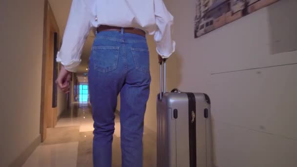 Woman walks down corridor of hotel and rolls suitcase with luggage on wheels. — Stock Video