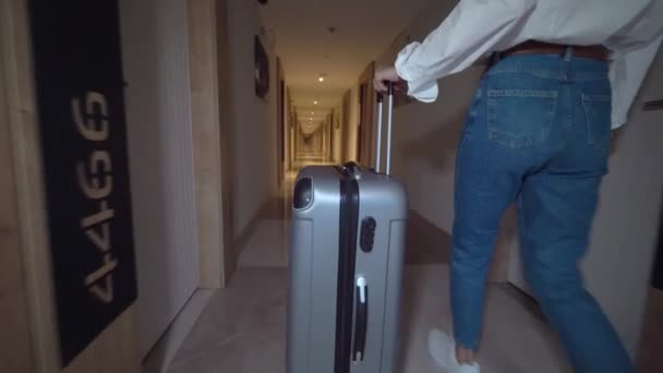 Woman walks down corridor of hotel and rolls suitcase with luggage on wheels. — Stock Video