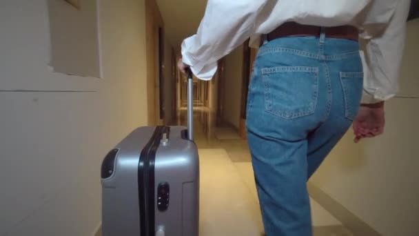 Woman walks down corridor of hotel and rolls suitcase with luggage on wheels. — Stock Video