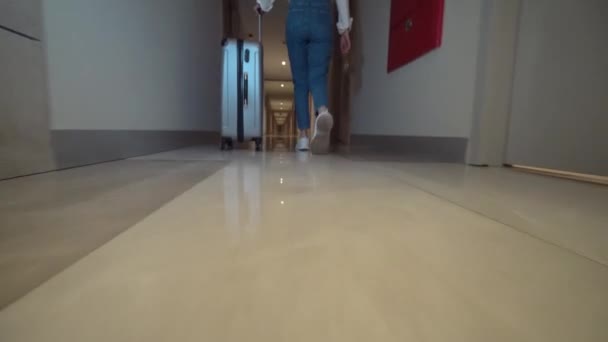 Zadní pohled na ženu kráčející chodbou hotelu. kutálí si zavazadla za sebou — Stock video