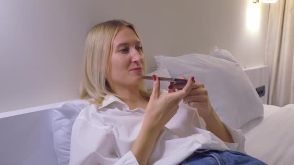 Žena doma nahrává hlasovou zprávu na svém smartphonu, zatímco leží na posteli. — Stock video