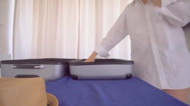 Beyaz gömlekli güzel bir kadın bavuldan bir şeyler çıkarır.