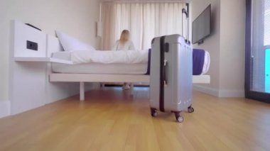 Turist bavuluyla apartmana giriyor, perdeleri itiyor ve manzaranın tadını çıkarıyor.