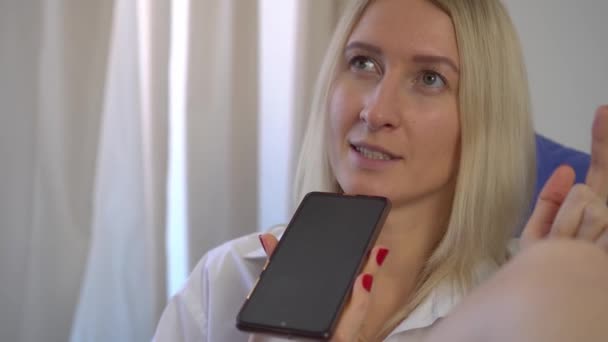 Een vrouw thuis registreert een voicemail op haar smartphone terwijl ze op bed ligt. — Stockvideo