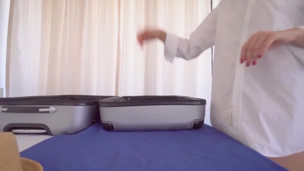 A young beautiful woman in a white shirt puts things out of a suitcase — Stock Video