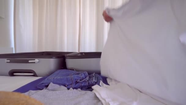 Eine junge schöne Frau im weißen Hemd sammelt Dinge in einem Koffer — Stockvideo