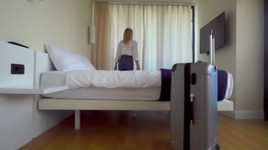 Turist bavuluyla apartmana giriyor, perdeleri itiyor ve manzaranın tadını çıkarıyor.