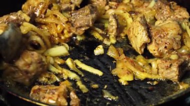 Bir kadının eli kızartma tavasında kızarmış domuz etini çevirir..