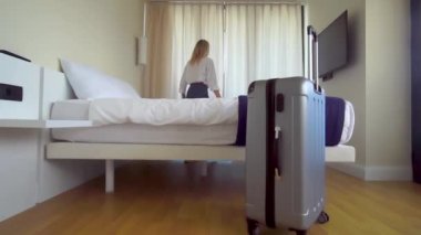 Turist bavuluyla apartmana giriyor, perdeleri itiyor ve manzaranın tadını çıkarıyor.