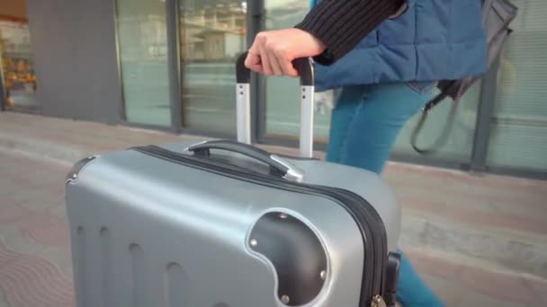 Close-up of woman leaving hotel with luggage. She rolls suitcase down street — Stock Video