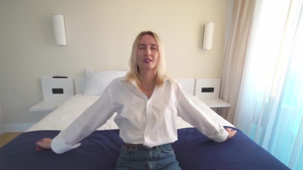 Een blondine in een wit shirt valt op een wit bed in slow motion. — Stockvideo