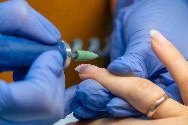 Mavi eldivenli manikür ustası jel cilası ve makrodan önce özel bir aletle tırnaklarını gıcırdatır..