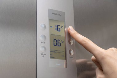 Bir kadının elinin yakın çekimi buzdolabının ısısını düzenler. Modern gri buzdolabı. Kadının eli sıcaklığı eksi on altı dereceye çıkarıyor.