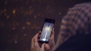 Kameraya arkası dönük duran kadın telefonuna kar yağışı yağdırıyor.
