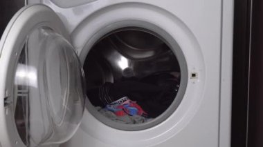 Kadın eli çamaşır, iç çamaşırı ve gardırop malzemelerini çamaşır makinesine yükler.