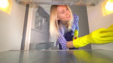 Boş bir buzdolabını temizleyen lastik eldivenli bir kadın..