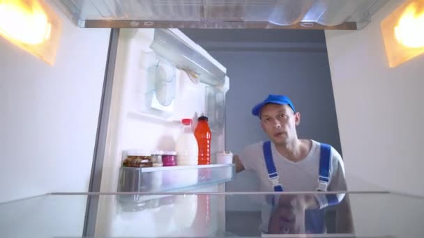 Ремонтник смотрит в холодильник, кладет руки на голову и удивляется — стоковое видео