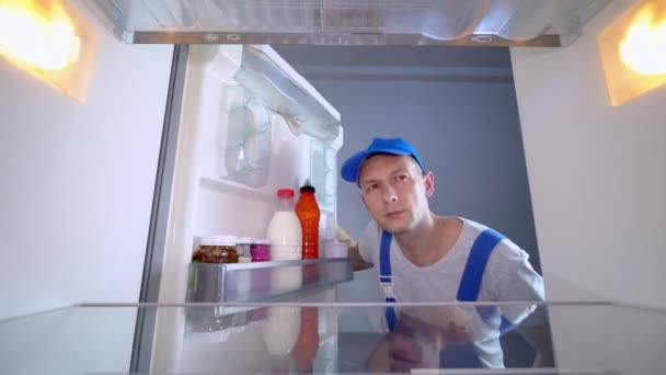 Ремонтник смотрит в холодильник, кладет руки на голову и удивляется — стоковое видео