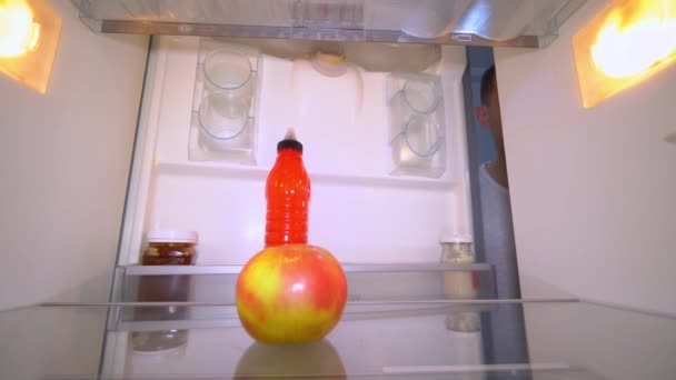 El muchacho abre el refrigerador, en que hay solamente una manzana. — Vídeos de Stock