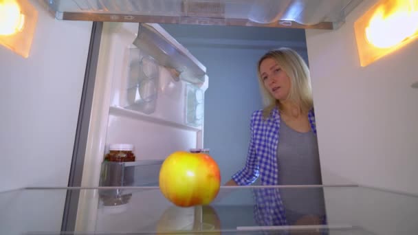 The woman opens the refrigerator, in which there is only an apple. She's upset. — Stock Video