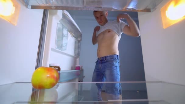 Guy opens the refrigerator where it's empty and points to his belly with fat. — Stock Video