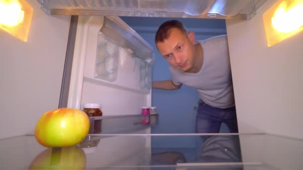 Der Kerl öffnet den Kühlschrank, in dem es nur einen Apfel gibt. — Stockvideo