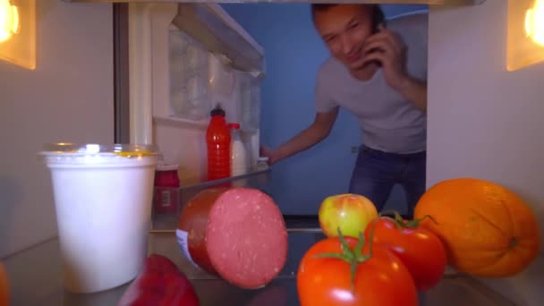 男は電話で冷蔵庫を開けてリンゴとトマトを取り出し. — ストック動画