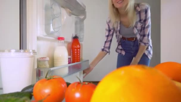 女の子は冷蔵庫を開けてオレンジを取り出します。内部からの眺め. — ストック動画