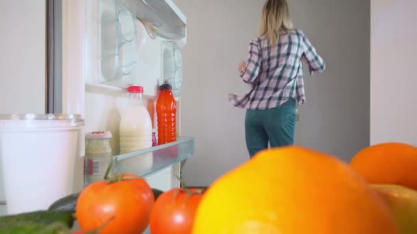 Γυναίκα με τζιν και πουκάμισο ανοίγει ψυγείο και χορεύει. Πυροβολισμοί από μέσα — Αρχείο Βίντεο
