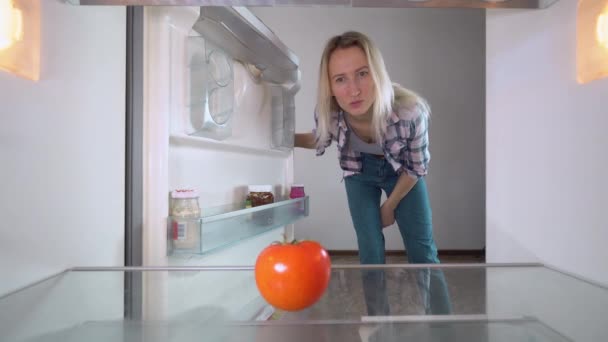 Eine Frau bestellt online Lebensmittel und blickt in einen leeren Kühlschrank. — Stockvideo