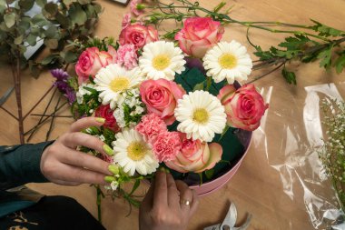 Genç bir kadın çiçekçinin elleri masanın üzerinde pembe güller ve beyaz papatyalar oluşturur.