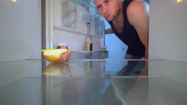 Человек смотрит в холодильник, нюхает лук и берет бутылку алкоголя. — стоковое видео