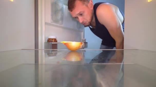 Der Mann öffnet den Kühlschrank und schaut hinein, im Regal steht eine Zwiebel. — Stockvideo