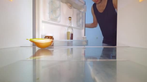 Человек смотрит в холодильник, смотрит на лук и берет бутылку алкоголя. — стоковое видео