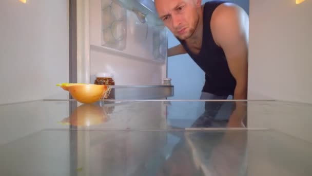 Man opent de koelkast en kijkt naar binnen, er staat een ui op de plank. — Stockvideo