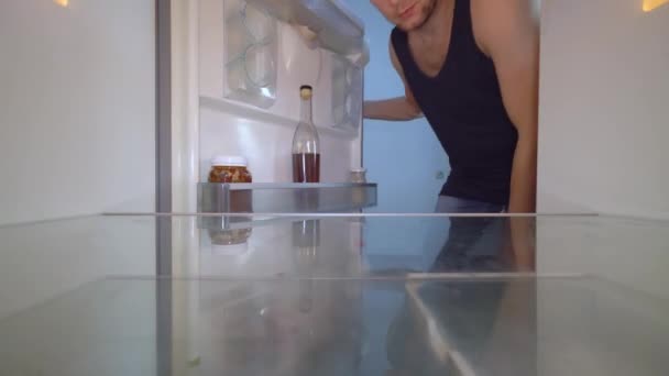 Omul se uită într-un frigider gol și scoate o sticlă de alcool. Alcoolismul — Videoclip de stoc