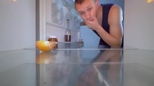 Человек смотрит в холодильник, смотрит на лук и берет бутылку алкоголя. — стоковое видео