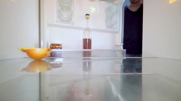 Hombre mira en el refrigerador, mira la cebolla y toma una botella de alcohol. — Vídeo de stock