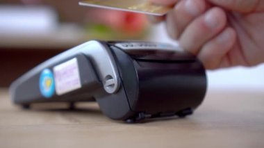 Bir adamın eli terminale plastik bir kart getirir ve bağlantısız ödeme yapar.