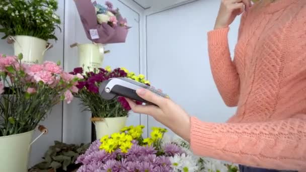 Kadın satıcı çiçeklerin arka planına karşı kredi kartını terminale uygular — Stok video