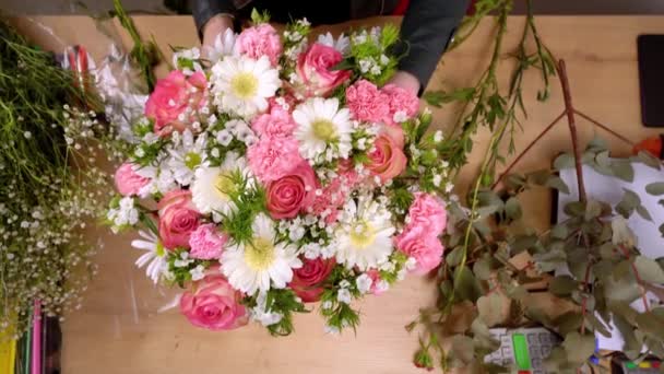 Primer plano de las manos de una florista femenina que empaca una hermosa composición — Vídeos de Stock