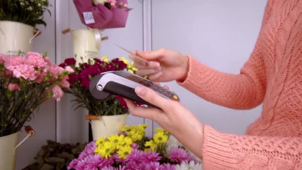 Жінка продавець застосовує кредитну картку до терміналу на тлі квітів — стокове відео