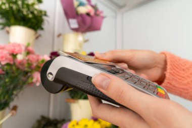 Çiçekçinin elindeki ödeme terminalinin yakın plan görüntüsü. Müşterinin eli, temassız bir kartla siparişin parasını ödüyor.