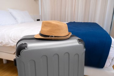 Otel odasında üzerinde hasır şapka olan gri bir valizin yakın çekimi. Seyahat, tatil kavramı
