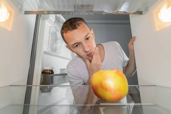 Niezadowolony Głodny Mężczyzna Szuka Jedzenia Lodówce Patrzy Zaskoczony Rdzeń Jabłka — Zdjęcie stockowe