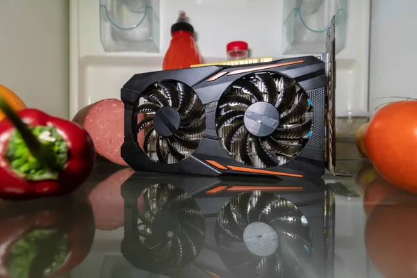 An overheated video card for mining or gaming on the refrigerator shelf with vegetables . Creative CPU cooling. Cryptocurrency Mining