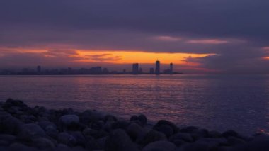 Tatil köyünün arka planında deniz ve gün batımı. Georgia 'da Batumi. Şehir, deniz kıyısında, kırmızı günbatımı güneşinde ve bulutlarda yer almaktadır. Yolculuk. Bulutlarda gün batımında şehrin silueti. Okyanus.