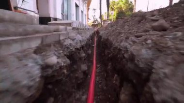 Yeni izole edilmiş internetin eve güvenli bağlantısı, gaz kartı, kırmızı metal banttan yapılmış sistemin inşaatı şehir caddesinde kazılmış çukurda bulunuyor. Üst görüntü, yerdeki dengeleyicide kamera hareketi.