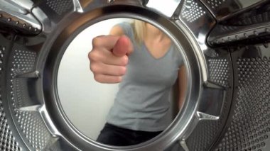 chamber is inside drum of washing machine. woman's hand shows fig and an obscene gesture, fuck you. woman puts her hand inside and shows that she is tired of doing laundry and cleaning. wants to rest